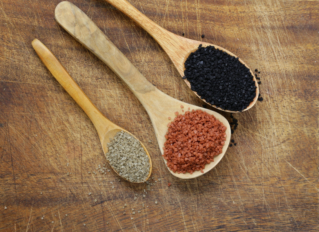 Wooden spoons of red, black and green Hawaiian sea salt on a cutting board